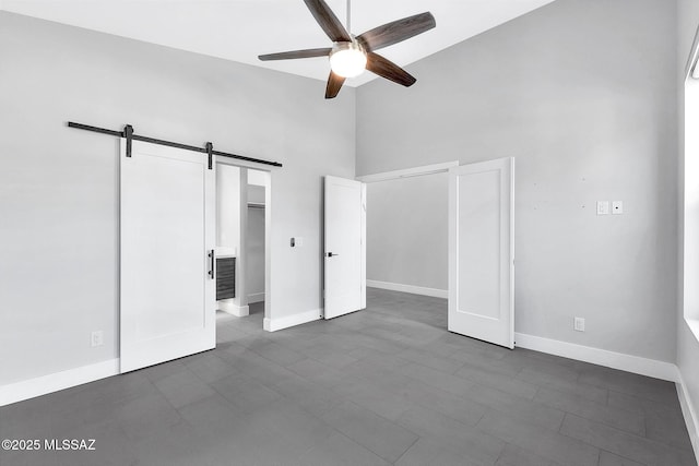 unfurnished bedroom with a barn door, ceiling fan, and ensuite bathroom