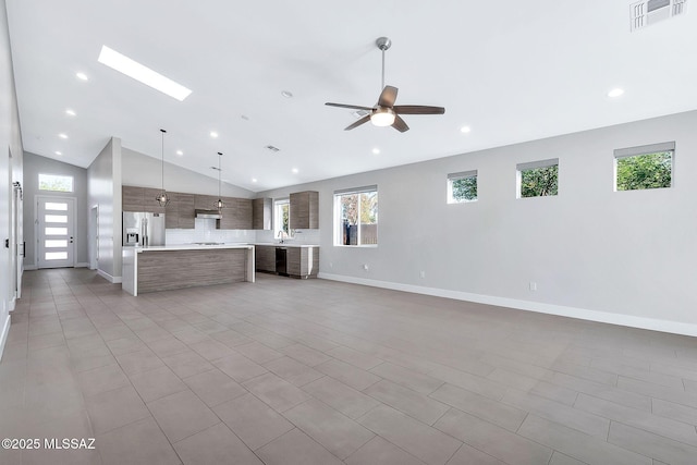 unfurnished living room with ceiling fan, lofted ceiling with skylight, sink, and light tile patterned floors