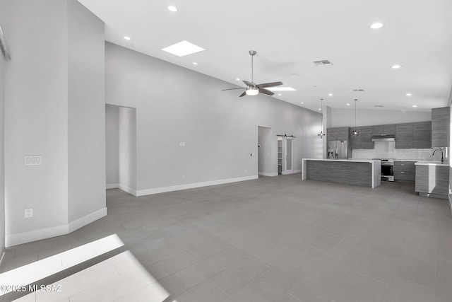 unfurnished living room featuring a barn door, sink, light tile patterned floors, and a towering ceiling