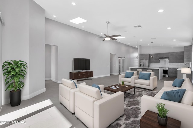 living room with sink, a skylight, a towering ceiling, ceiling fan, and a barn door