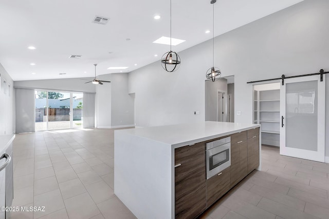 kitchen with decorative light fixtures, stainless steel microwave, a kitchen island, ceiling fan, and a barn door