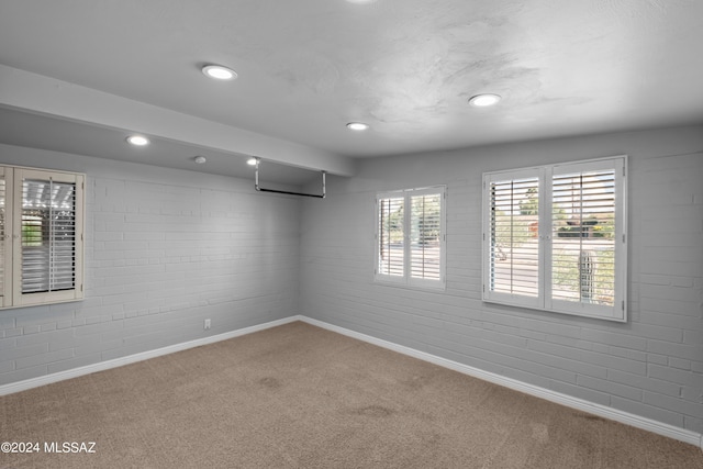 carpeted empty room featuring brick wall