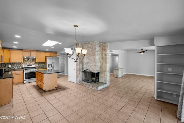 kitchen featuring ceiling fan with notable chandelier, appliances with stainless steel finishes, a center island, a fireplace, and hanging light fixtures