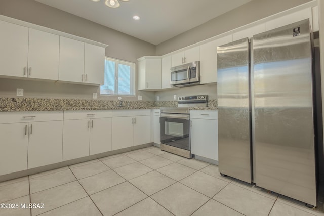 kitchen featuring stainless steel appliances, light tile patterned floors, white cabinets, and light stone counters