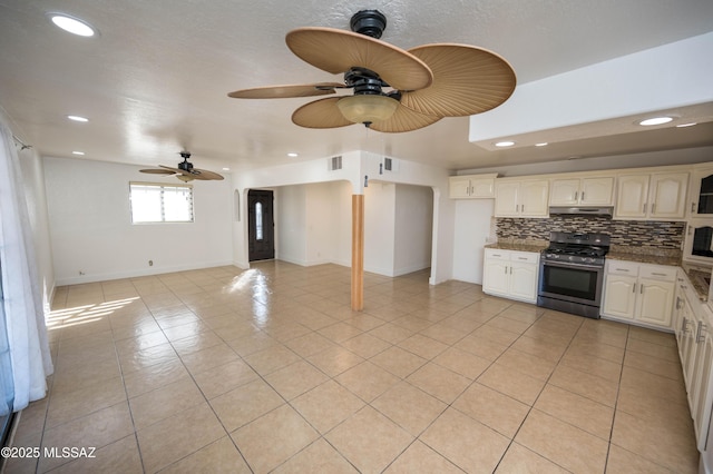 kitchen featuring dark stone counters, tasteful backsplash, stainless steel gas stove, ceiling fan, and light tile patterned floors