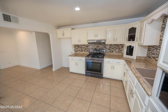 kitchen featuring sink, light tile patterned floors, light stone counters, stainless steel gas range oven, and decorative backsplash