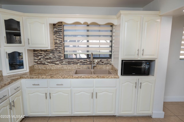 kitchen featuring sink, backsplash, white cabinets, light tile patterned floors, and light stone counters