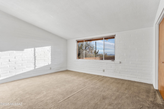 carpeted empty room with vaulted ceiling, a textured ceiling, and brick wall