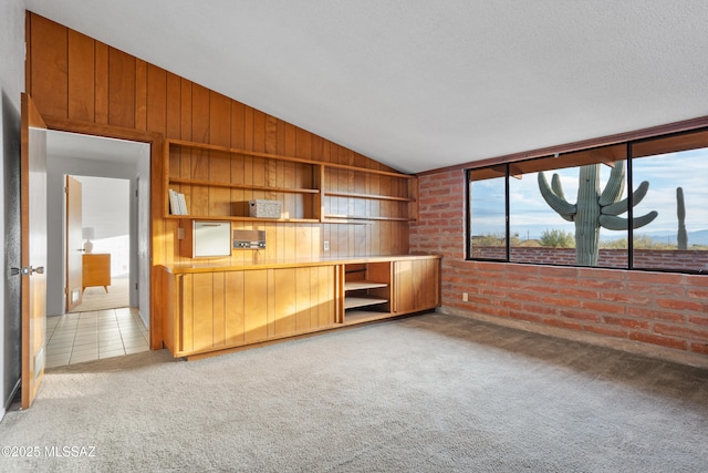 unfurnished living room with light tile patterned floors, light carpet, brick wall, wood walls, and vaulted ceiling