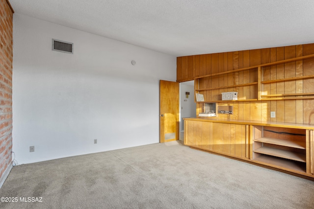 interior space featuring vaulted ceiling, a textured ceiling, carpet, and visible vents