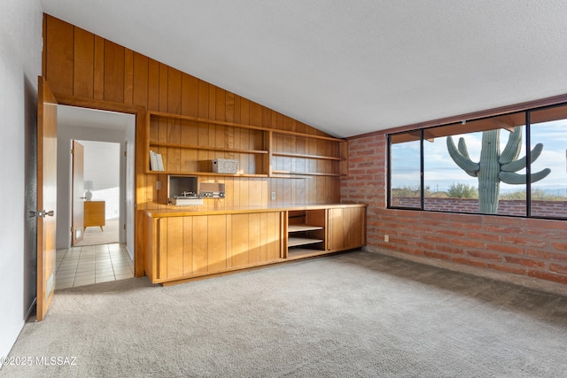 unfurnished living room with lofted ceiling, light tile patterned floors, wooden walls, light colored carpet, and brick wall