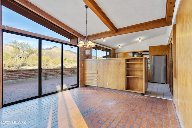 empty room with lofted ceiling with beams, brick floor, a mountain view, and a notable chandelier