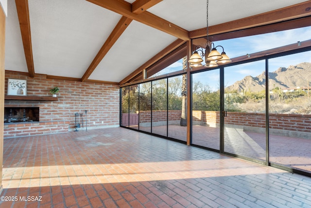 unfurnished sunroom with vaulted ceiling with beams, an inviting chandelier, a brick fireplace, and a mountain view