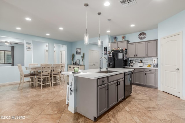 kitchen featuring gray cabinets, pendant lighting, sink, a kitchen island with sink, and black appliances