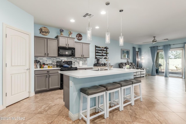 kitchen featuring sink, gray cabinets, pendant lighting, a kitchen island with sink, and black appliances