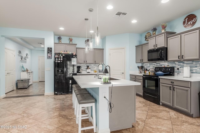 kitchen featuring sink, gray cabinetry, a center island with sink, pendant lighting, and black appliances