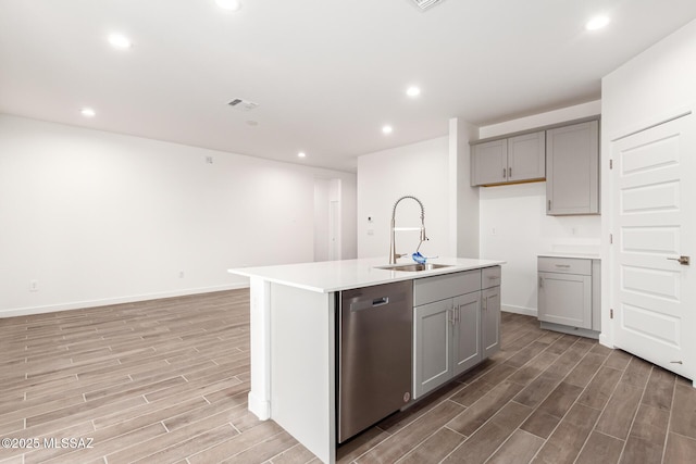 kitchen with gray cabinets, light hardwood / wood-style floors, stainless steel dishwasher, sink, and an island with sink