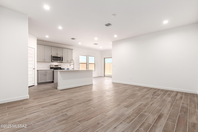 kitchen featuring appliances with stainless steel finishes, gray cabinetry, a kitchen island with sink, and sink