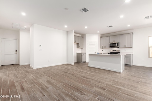 kitchen with stainless steel appliances, an island with sink, light hardwood / wood-style floors, sink, and gray cabinetry