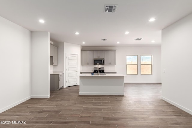 kitchen with sink, gray cabinets, stainless steel appliances, and a center island with sink