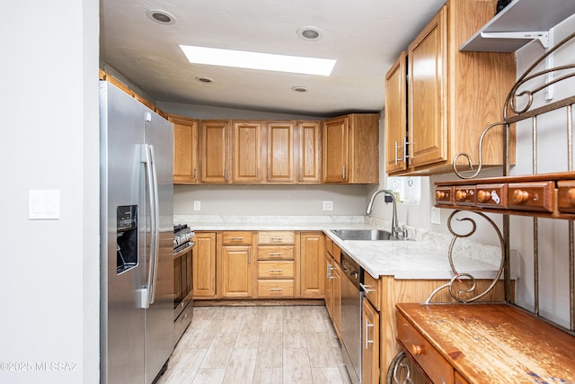 kitchen featuring sink, lofted ceiling with skylight, stainless steel appliances, and light wood-type flooring