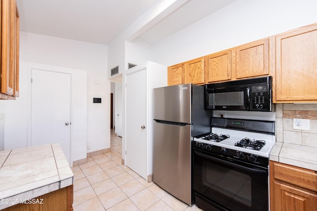 kitchen featuring stainless steel fridge, tile counters, backsplash, light tile patterned flooring, and gas range oven