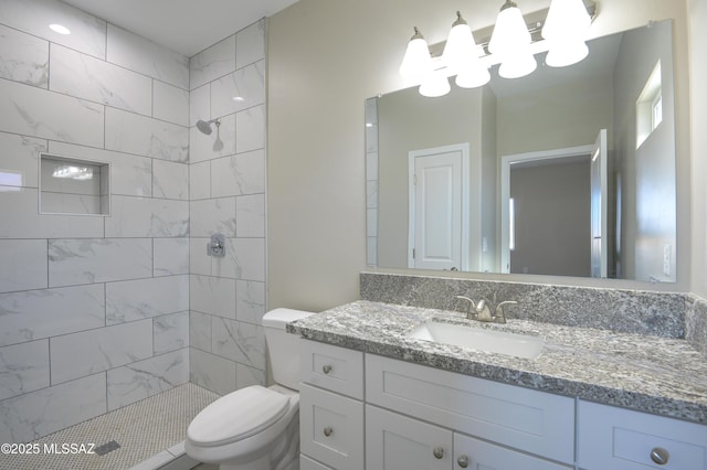 bathroom with toilet, tiled shower, and vanity