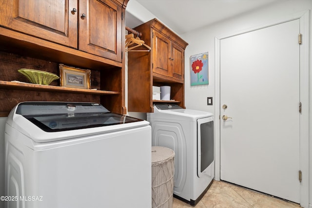 clothes washing area with washing machine and dryer, cabinets, and light tile patterned floors