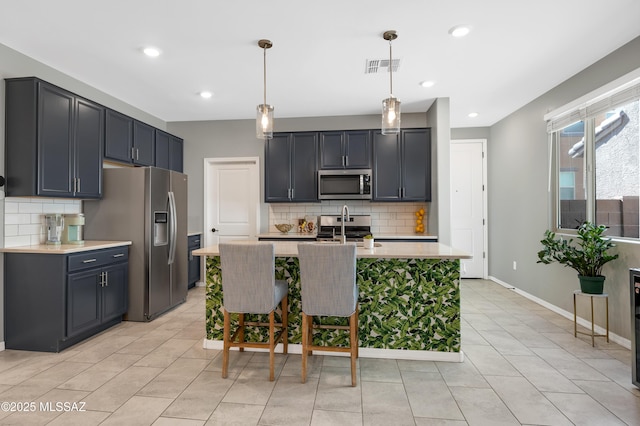 kitchen featuring sink, appliances with stainless steel finishes, decorative backsplash, a center island with sink, and decorative light fixtures