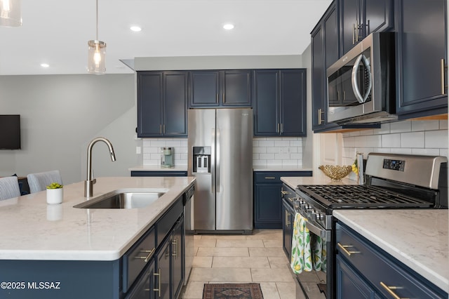 kitchen featuring decorative light fixtures, blue cabinetry, an island with sink, and appliances with stainless steel finishes