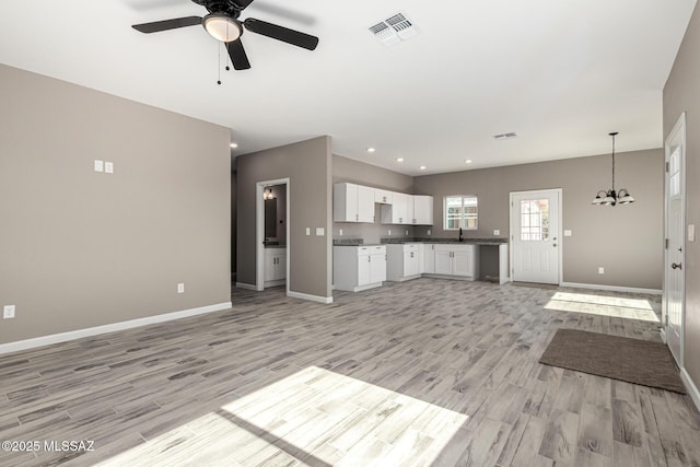 unfurnished living room featuring ceiling fan with notable chandelier and light wood-type flooring