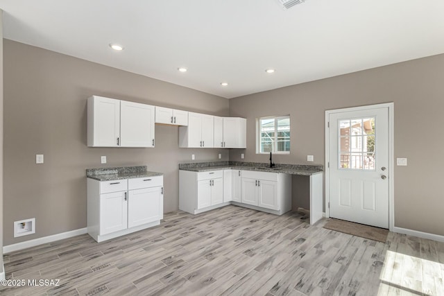 kitchen featuring sink, stone countertops, white cabinetry, and light hardwood / wood-style flooring