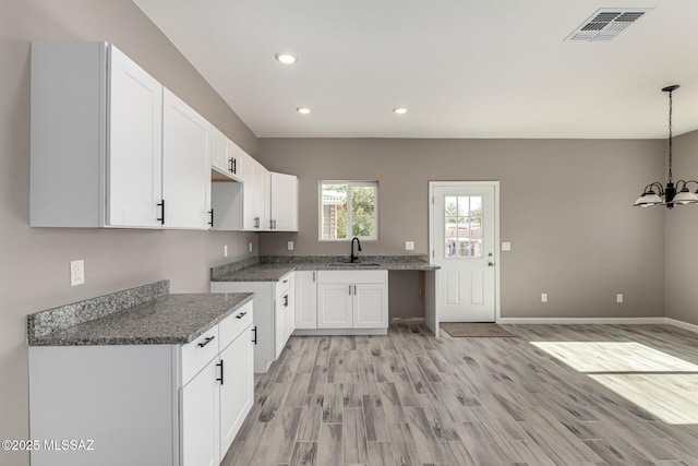 kitchen featuring sink, white cabinetry, dark stone counters, and hanging light fixtures