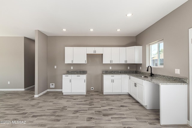 kitchen featuring light stone countertops, light hardwood / wood-style floors, white cabinets, and sink