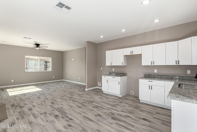 kitchen featuring light wood-type flooring, ceiling fan, white cabinets, and light stone counters