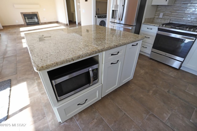 kitchen with washer / clothes dryer, white cabinetry, appliances with stainless steel finishes, and tasteful backsplash