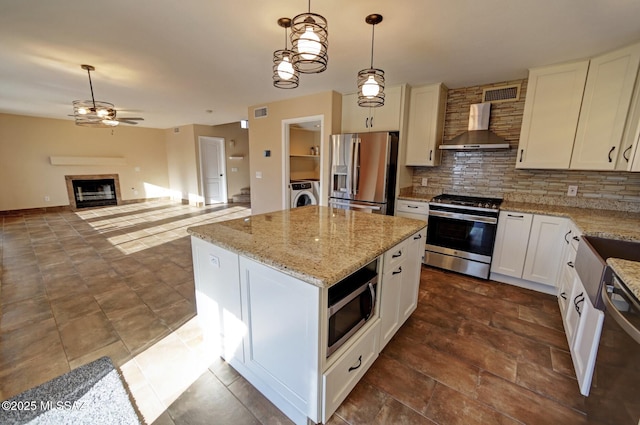 kitchen featuring pendant lighting, appliances with stainless steel finishes, wall chimney exhaust hood, white cabinets, and a center island