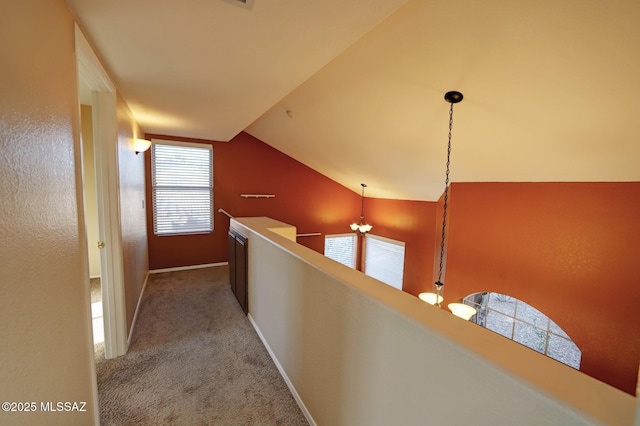 corridor with carpet floors, an inviting chandelier, and vaulted ceiling