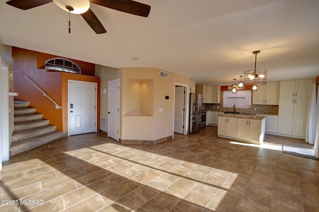 interior space with a center island, tasteful backsplash, stainless steel fridge with ice dispenser, hanging light fixtures, and sink