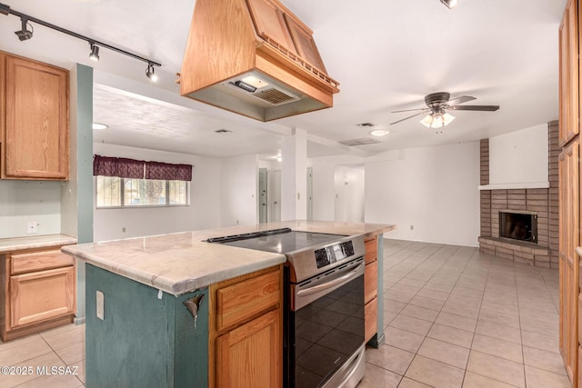 kitchen featuring a center island, light tile patterned floors, electric range, ceiling fan, and a brick fireplace