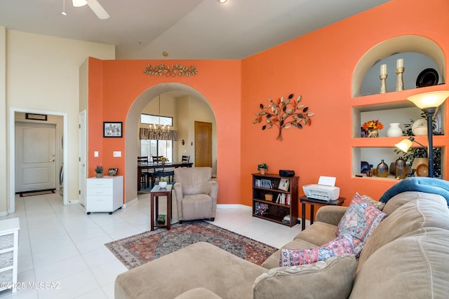 tiled living room featuring high vaulted ceiling, ceiling fan with notable chandelier, and built in features