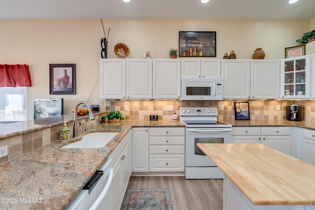 kitchen with white cabinetry, sink, light wood-type flooring, backsplash, and white appliances