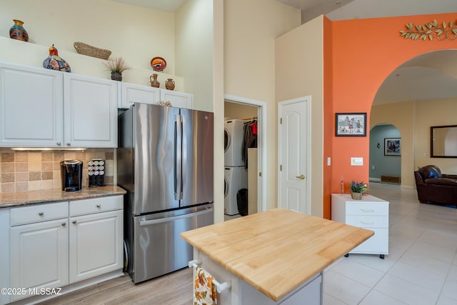 kitchen featuring stainless steel refrigerator, stacked washer and clothes dryer, light stone counters, white cabinets, and decorative backsplash