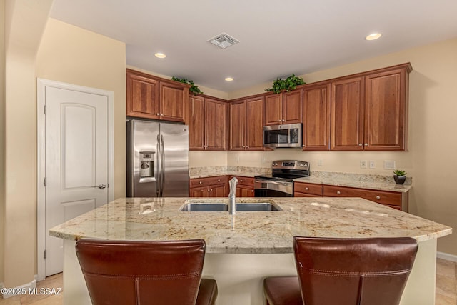 kitchen with light stone countertops, a kitchen breakfast bar, stainless steel appliances, and an island with sink