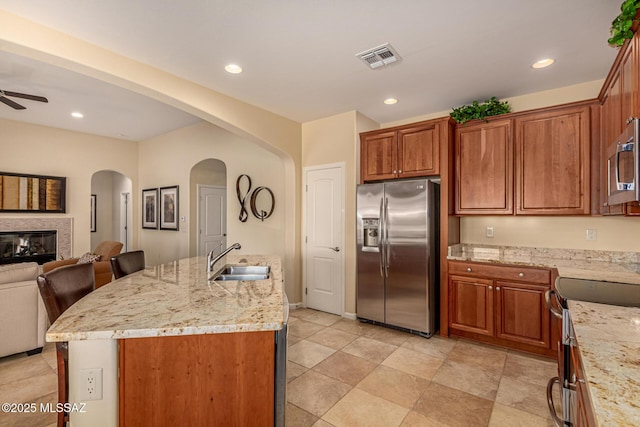 kitchen with stainless steel appliances, sink, light stone countertops, and an island with sink