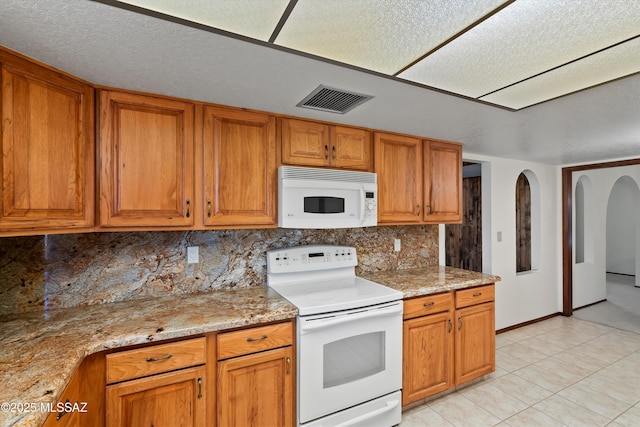 kitchen with light stone counters, backsplash, white appliances, and light tile patterned floors