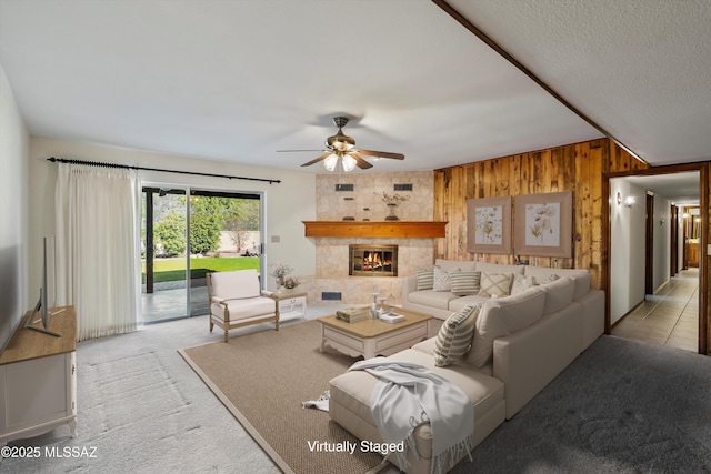 carpeted living room with ceiling fan, a textured ceiling, a tile fireplace, and wood walls