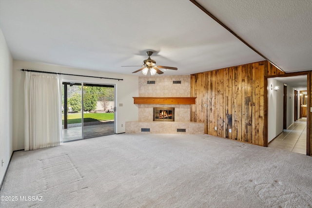 unfurnished living room featuring light carpet, wood walls, a tiled fireplace, and ceiling fan