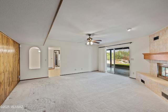 unfurnished living room with ceiling fan, wood walls, light colored carpet, and a fireplace