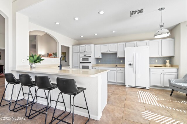 kitchen with pendant lighting, sink, backsplash, white cabinetry, and white appliances